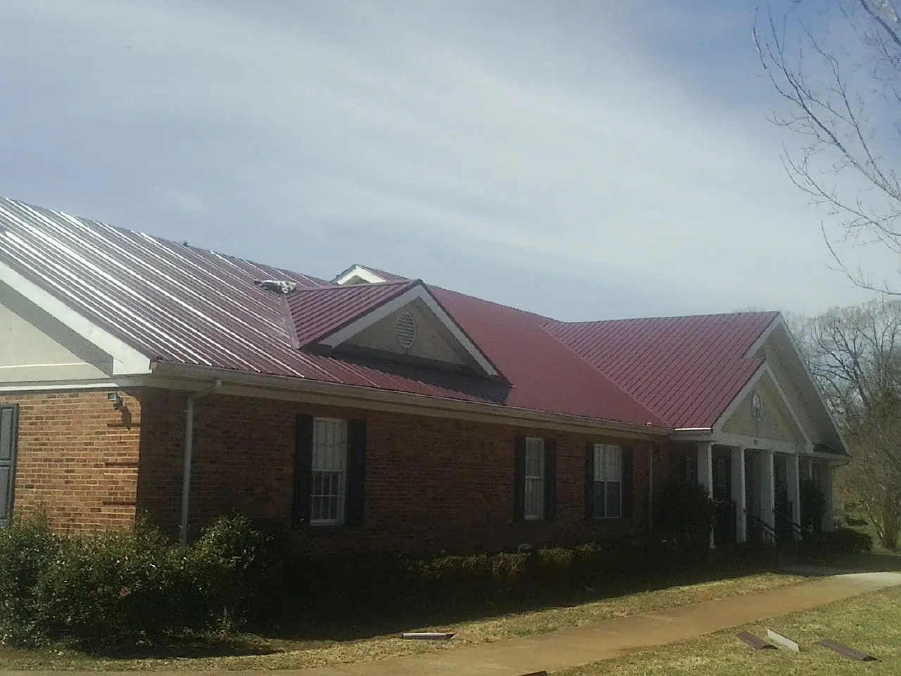 Red metal roof with gabled entries on a long brick building, from a Hail Damage Roof Repair job in Straughn
