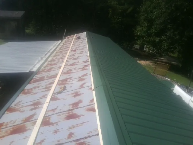 Old rusted panels beside newly installed green metal roofing — Wind Damage Roof Repair by Roofing Brothers in Straughn