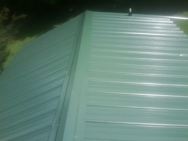 New green metal panels meeting at the ridge of a roof — Flat Roof Repair work by our crew in Straughn
