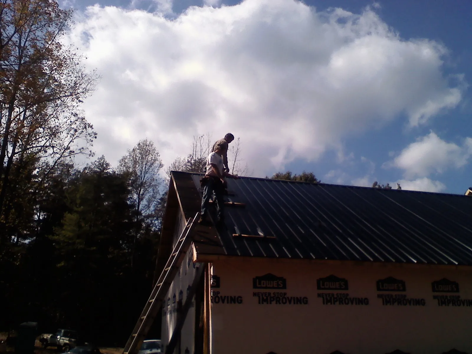 Roofer fastening dark metal panels high against a cloudy sky, from a Roof Inspection job in Straughn
