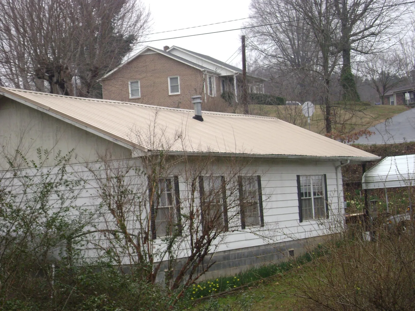 Tan metal roof on a white sided house set into a hillside — Commercial Roofing by Roofing Brothers in Straughn